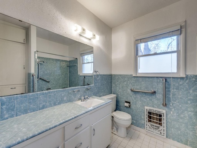 bathroom with heating unit, toilet, vanity, tiled shower, and tile patterned floors