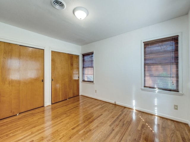 unfurnished bedroom with multiple windows, visible vents, multiple closets, and wood finished floors