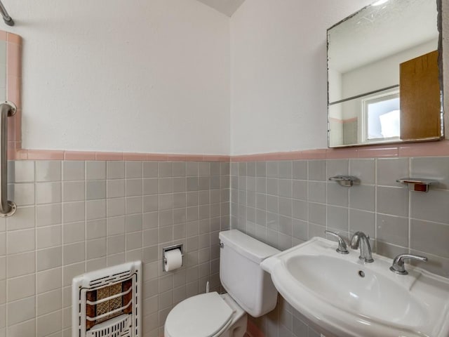 bathroom featuring toilet, a sink, tile walls, wainscoting, and heating unit