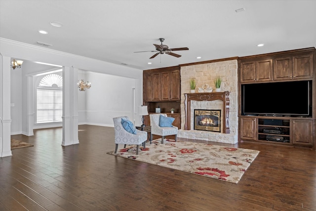 living area featuring dark wood-style floors, crown molding, visible vents, a ceiling fan, and a stone fireplace