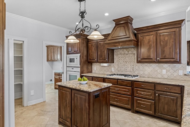 kitchen with pendant lighting, custom range hood, backsplash, ornamental molding, and white appliances