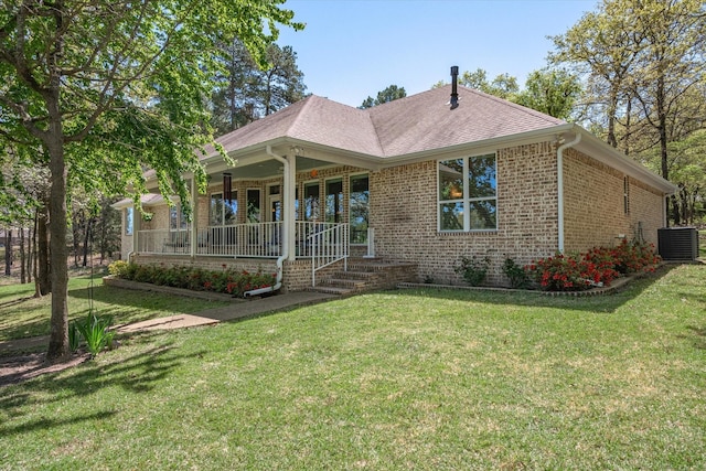 view of front of home featuring brick siding, roof with shingles, covered porch, a front yard, and cooling unit