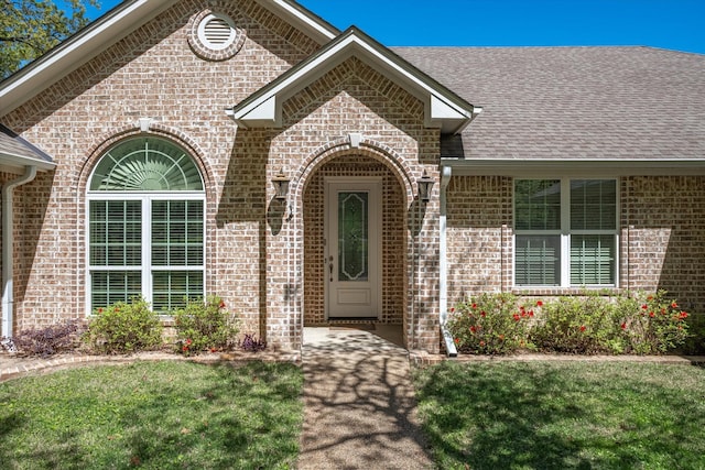 property entrance with a shingled roof, a lawn, and brick siding