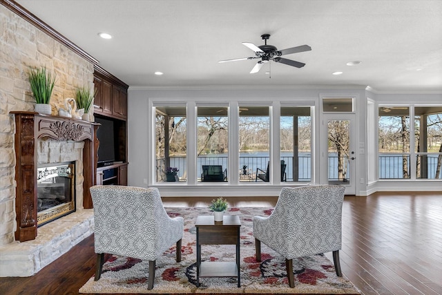 interior space with ornamental molding, a stone fireplace, dark wood-style flooring, and recessed lighting