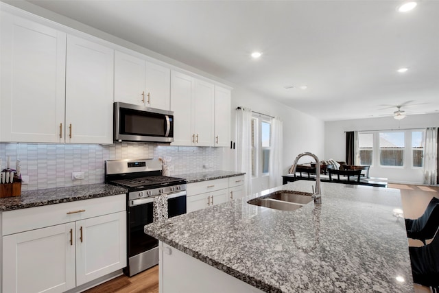 kitchen featuring a sink, white cabinets, appliances with stainless steel finishes, decorative backsplash, and dark stone counters