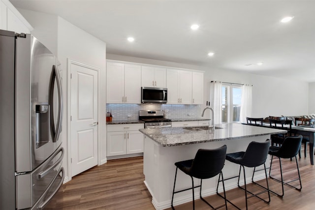 kitchen with light stone counters, a breakfast bar, wood finished floors, stainless steel appliances, and a sink