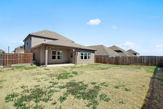 back of house with brick siding, a fenced backyard, a yard, and a patio