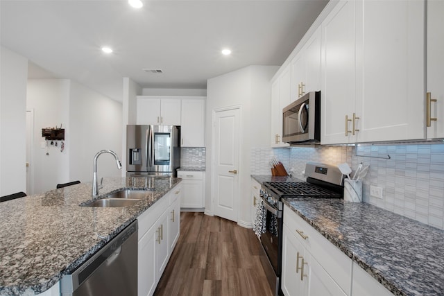 kitchen featuring stainless steel appliances, dark wood-style flooring, a sink, white cabinets, and dark stone countertops