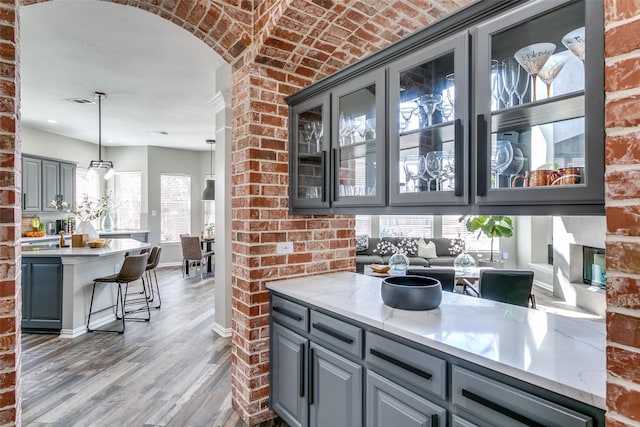 kitchen with gray cabinetry, brick wall, wood finished floors, baseboards, and glass insert cabinets