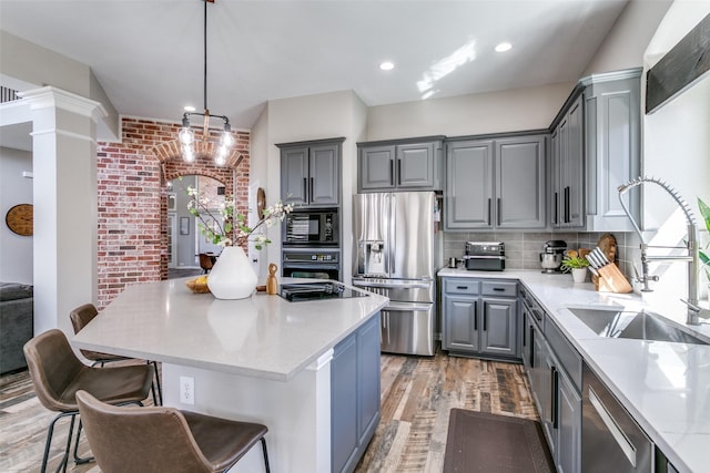 kitchen with light wood finished floors, ornate columns, gray cabinets, black appliances, and a sink