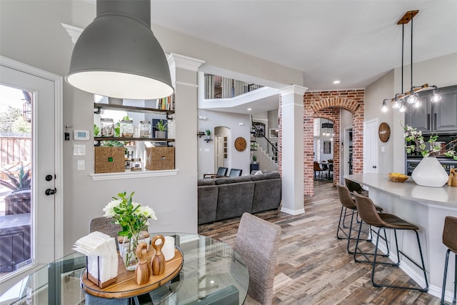 dining area featuring arched walkways, stairway, wood finished floors, and decorative columns