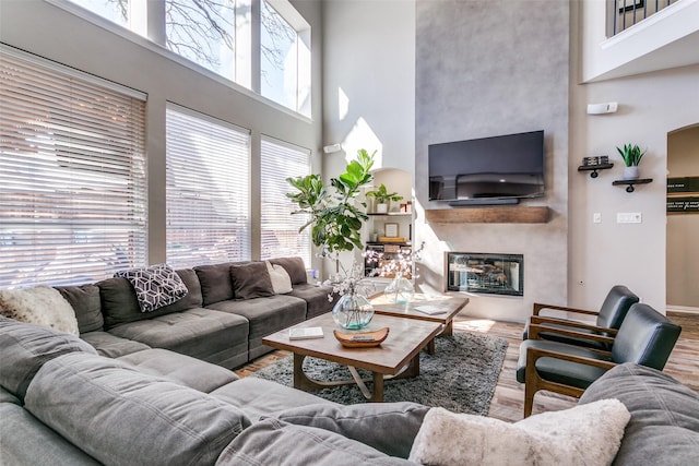 living area featuring a high ceiling, wood finished floors, and a glass covered fireplace