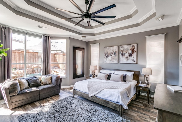 bedroom with ceiling fan, wood finished floors, visible vents, ornamental molding, and a tray ceiling