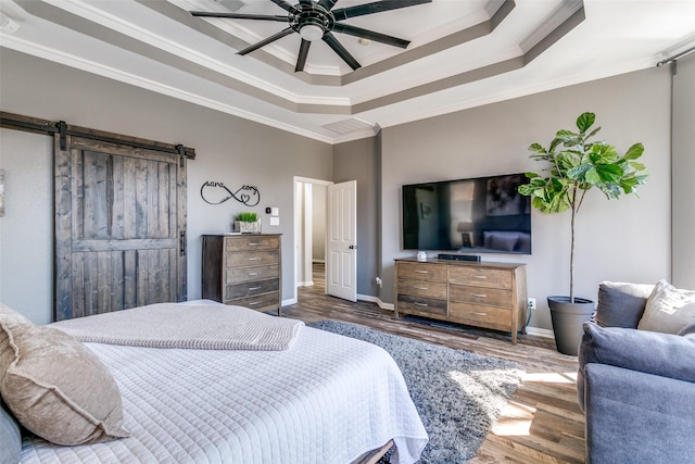 bedroom featuring crown molding, a raised ceiling, a barn door, wood finished floors, and baseboards