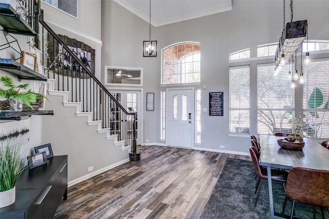 entrance foyer with a towering ceiling, ornamental molding, wood finished floors, stairs, and a chandelier