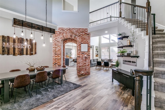 dining area featuring arched walkways, a high ceiling, wood finished floors, ornate columns, and stairs