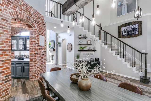 dining room featuring arched walkways, wood finished floors, a towering ceiling, baseboards, and stairs