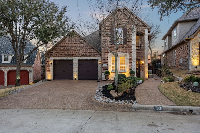 traditional home featuring stone siding, a garage, brick siding, and driveway