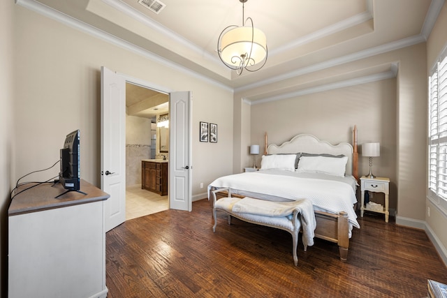 bedroom featuring visible vents, a tray ceiling, ornamental molding, wood finished floors, and ensuite bath