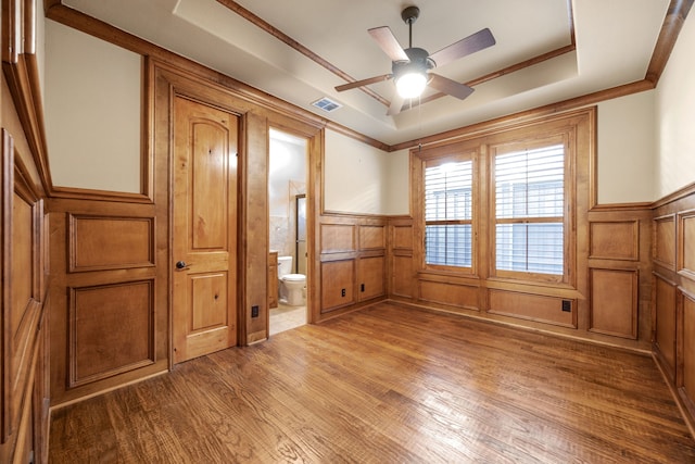 unfurnished bedroom with visible vents, wainscoting, a raised ceiling, and wood finished floors