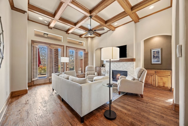 living area featuring dark wood-type flooring, a high ceiling, a tiled fireplace, and coffered ceiling