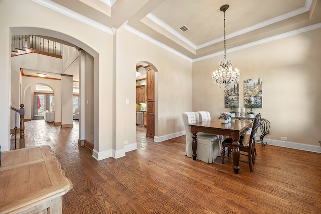 dining space with wood finished floors, baseboards, a tray ceiling, arched walkways, and ornamental molding