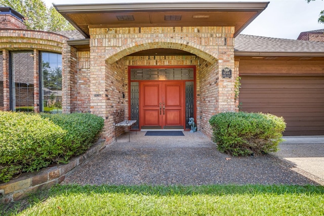 doorway to property with an attached garage, brick siding, and a shingled roof