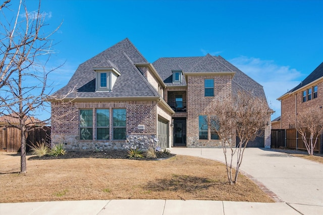 view of front of property with driveway, roof with shingles, fence, a front yard, and brick siding