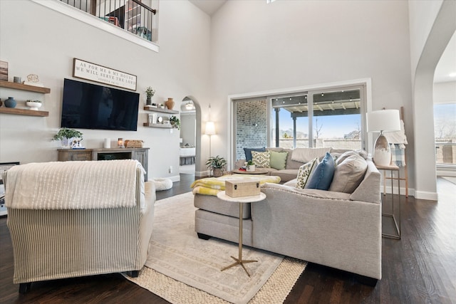 living room featuring a towering ceiling, baseboards, arched walkways, and wood finished floors