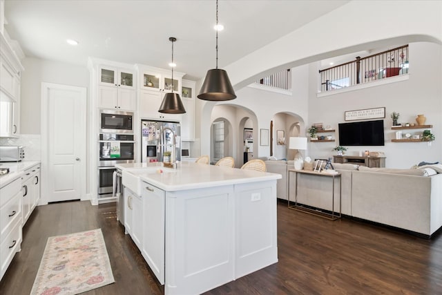 kitchen with dark wood-style floors, arched walkways, light countertops, glass insert cabinets, and white cabinets