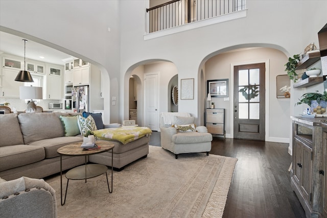 living room with a high ceiling, baseboards, and dark wood-type flooring