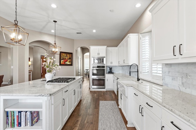 kitchen featuring visible vents, a center island, appliances with stainless steel finishes, arched walkways, and a notable chandelier