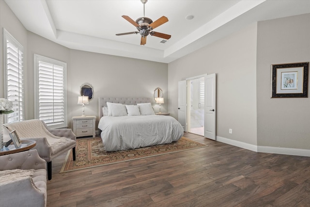 bedroom featuring a ceiling fan, wood finished floors, baseboards, visible vents, and a tray ceiling