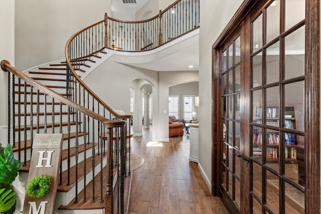 entrance foyer featuring wood finished floors, french doors, arched walkways, a high ceiling, and stairs