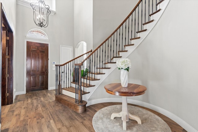 foyer with baseboards, a notable chandelier, wood finished floors, and stairs