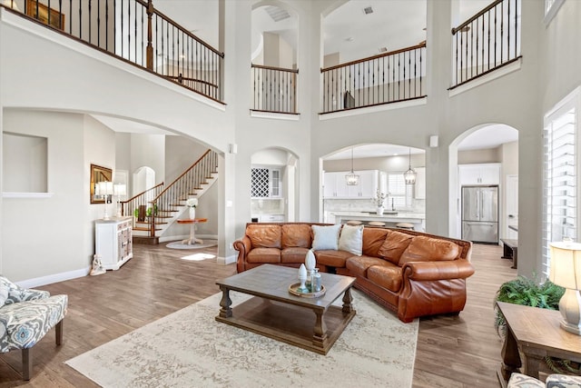 living room featuring arched walkways, stairs, baseboards, and wood finished floors