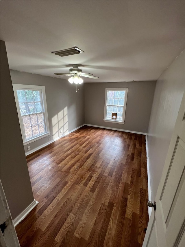 empty room with plenty of natural light, baseboards, and dark wood finished floors