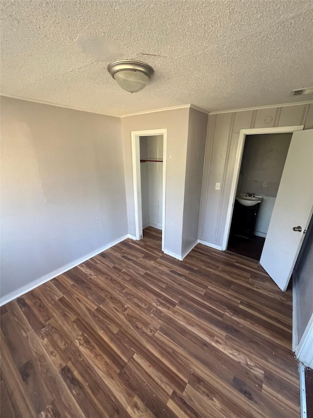 unfurnished bedroom with a textured ceiling, dark wood finished floors, baseboards, visible vents, and a closet