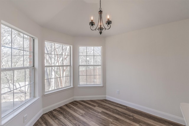 unfurnished dining area with plenty of natural light, baseboards, dark wood finished floors, and a notable chandelier