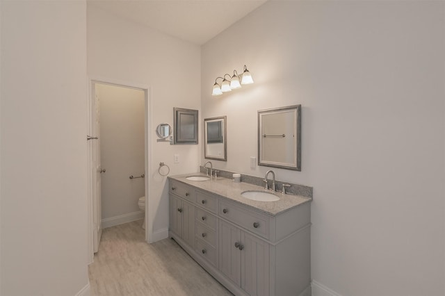 full bath with toilet, double vanity, baseboards, and a sink