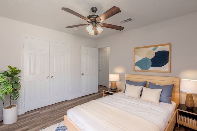 bedroom with baseboards, visible vents, ceiling fan, wood finished floors, and a closet