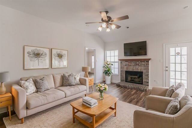 living area with ceiling fan, a fireplace, wood finished floors, baseboards, and vaulted ceiling