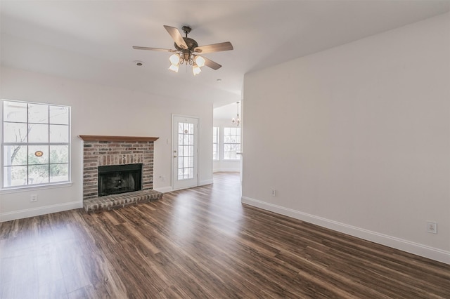 unfurnished living room featuring a brick fireplace, baseboards, dark wood-style floors, and ceiling fan with notable chandelier