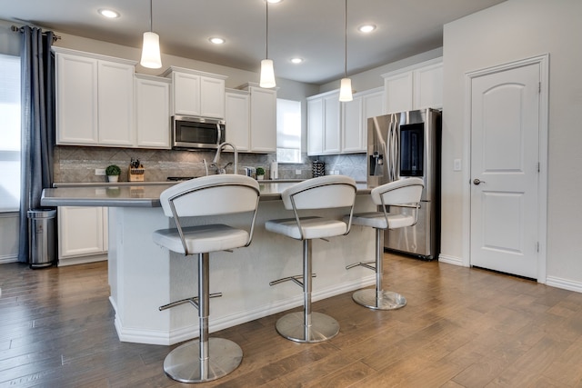 kitchen featuring appliances with stainless steel finishes, white cabinetry, a center island with sink, and dark wood-style floors