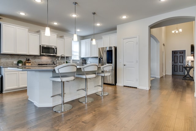 kitchen with stainless steel appliances, an island with sink, dark wood finished floors, and white cabinetry