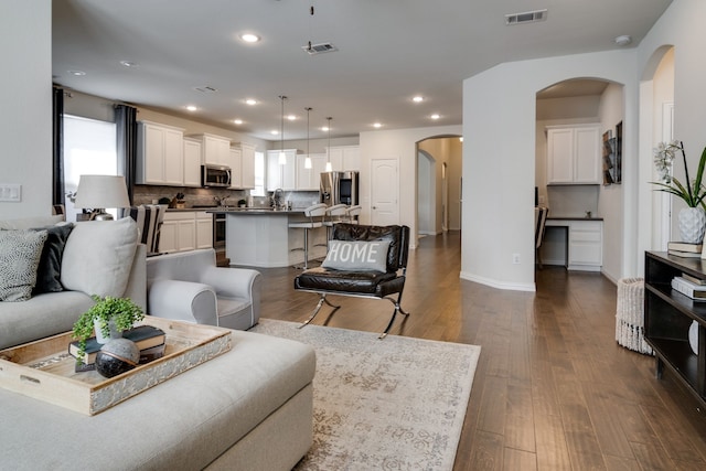 living room with dark wood-type flooring, arched walkways, visible vents, and recessed lighting