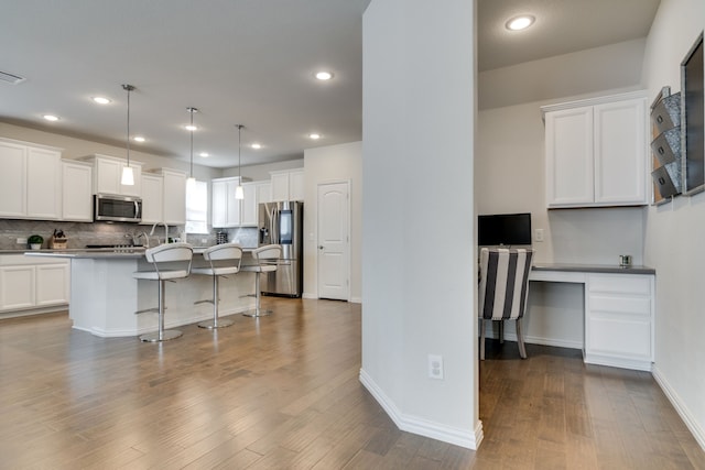 kitchen with decorative backsplash, a kitchen breakfast bar, wood finished floors, stainless steel appliances, and white cabinetry