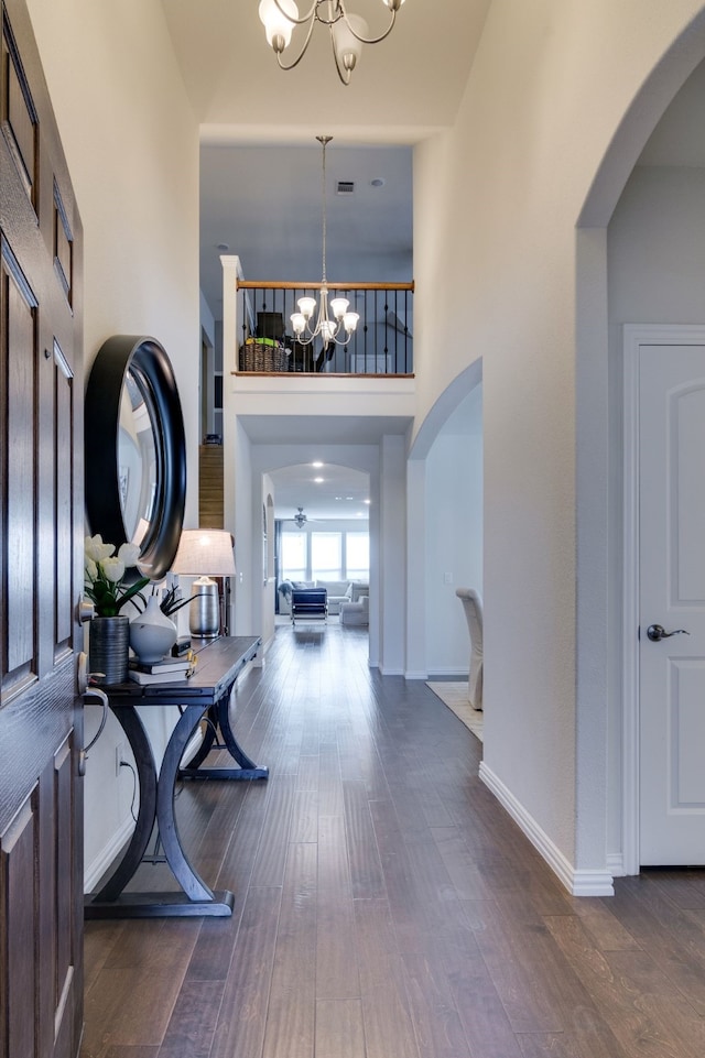 foyer with arched walkways, dark wood-type flooring, a high ceiling, and an inviting chandelier