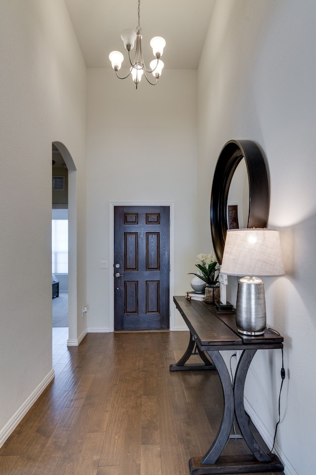 foyer entrance with arched walkways, wood-type flooring, a towering ceiling, an inviting chandelier, and baseboards