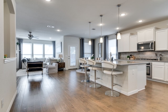 kitchen with appliances with stainless steel finishes, a kitchen breakfast bar, dark wood-style floors, and tasteful backsplash